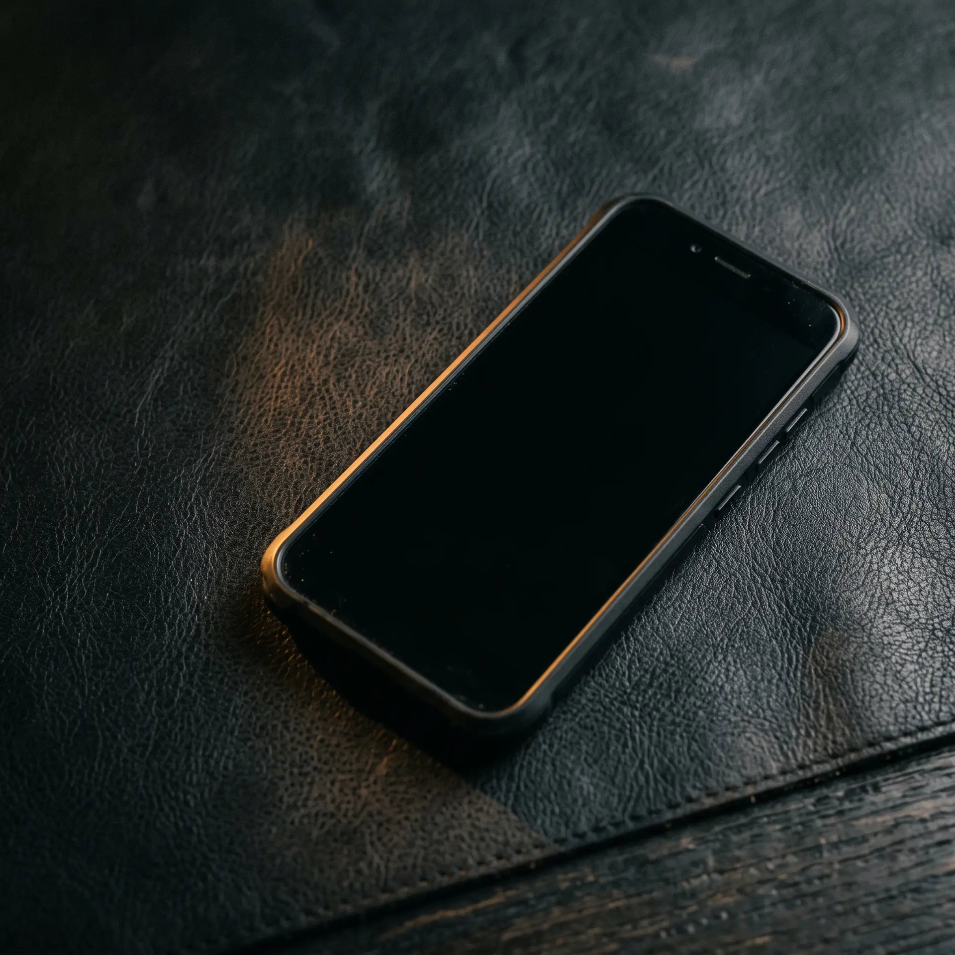 A phone lying flat and angled on a dark surface, screen blank